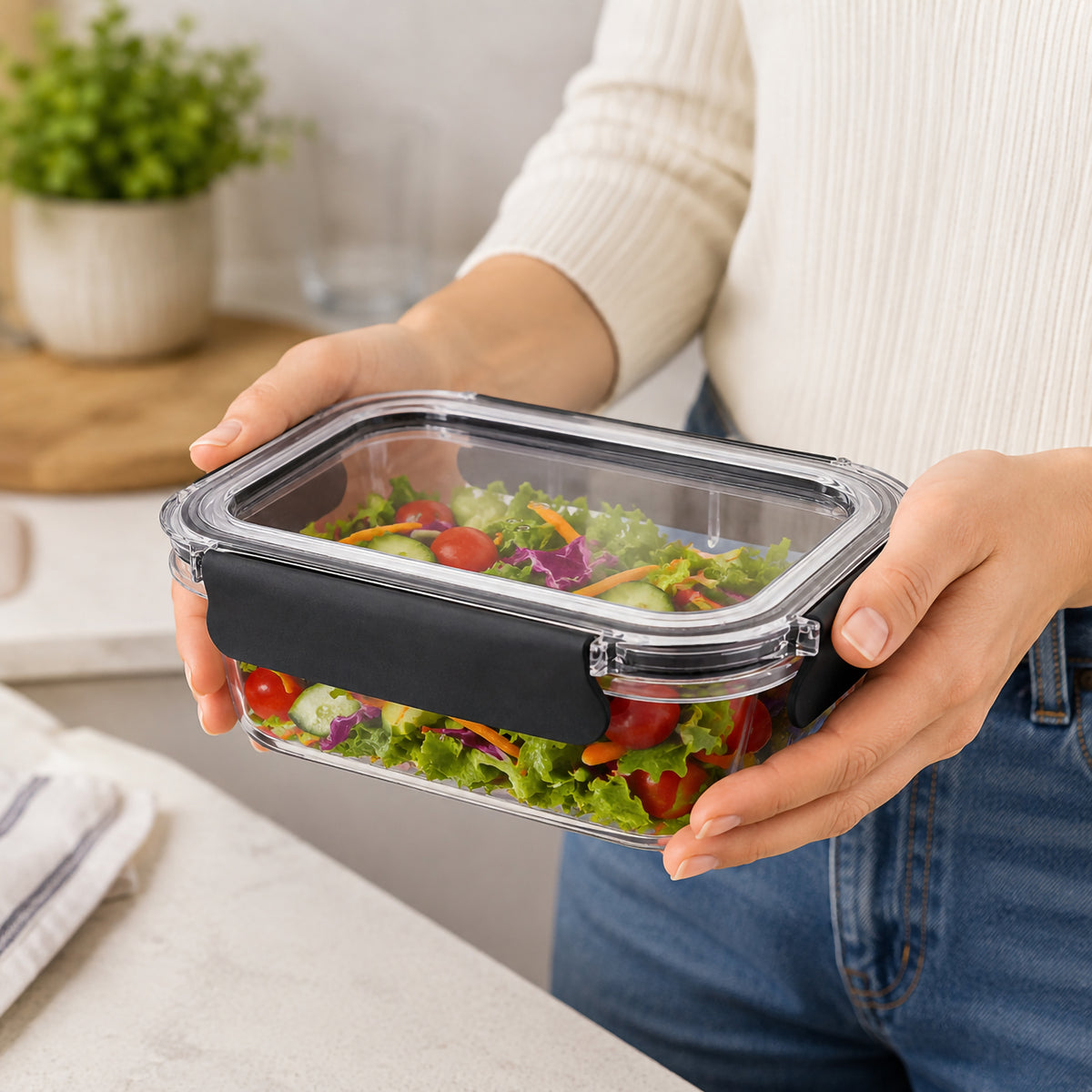 Italplast 950ml clear Snap Lock Food Container held securely in both hands and filled with a colourful fresh salad. The image highlights the transparent rectangular body, clear fitted lid and contrasting black snap lock closures, demonstrating a practical size for taking prepared lunches, salads and individual meals to work or study.