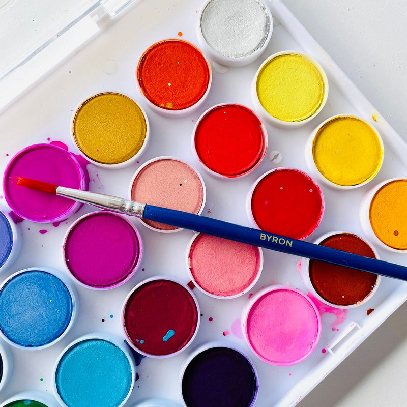 Close up of Jasart Byron watercolour discs in pinks, reds, yellows and blues with a blue Byron paint brush resting across the palette