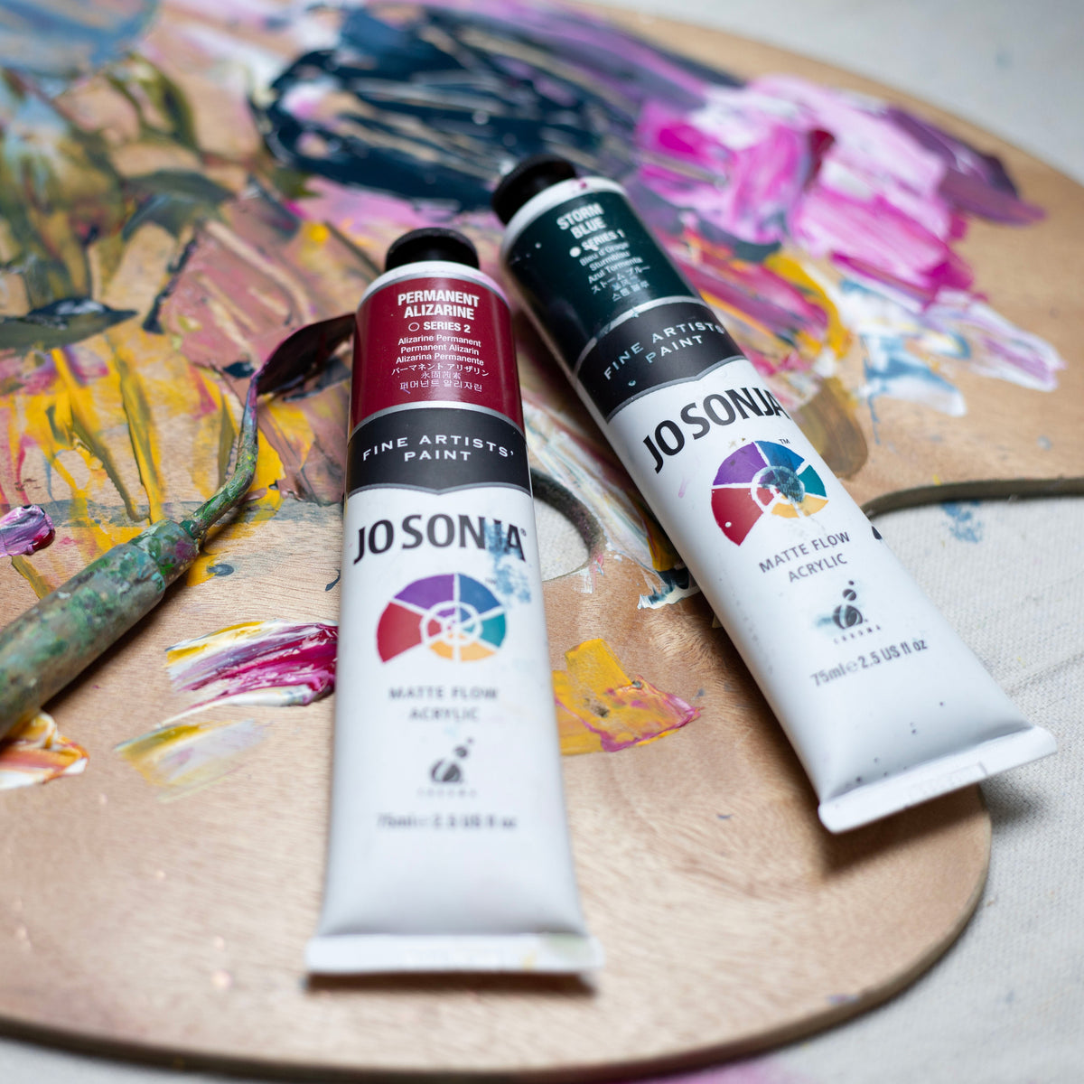 Two Jo Sonja's tubes resting on a paint smeared palette, range photo shown with Carbon Black