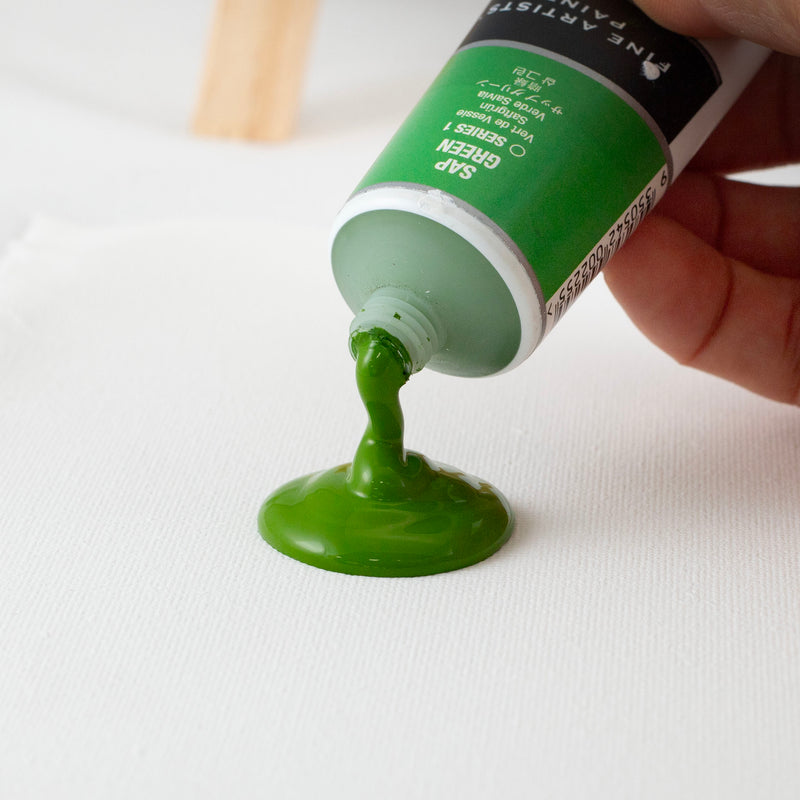 Hand squeezing Jo Sonja's Sap Green from the tube into a green pool on white canvas
