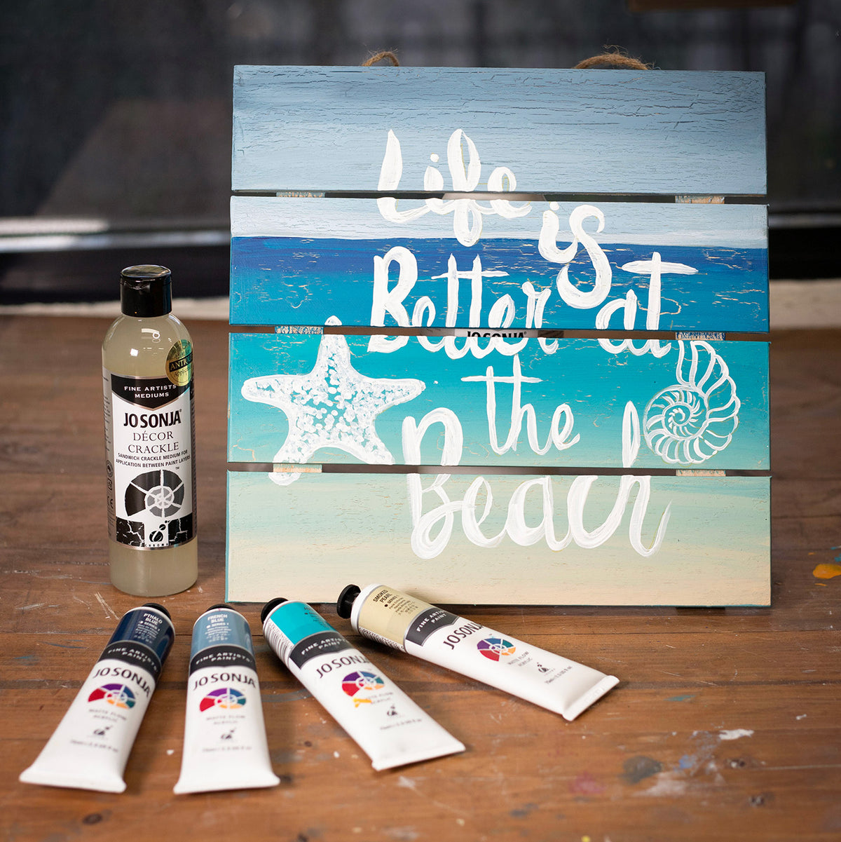 Hand painted Life is Better at the Beach sign with Jo Sonja tubes and a Decor Crackle bottle on a table