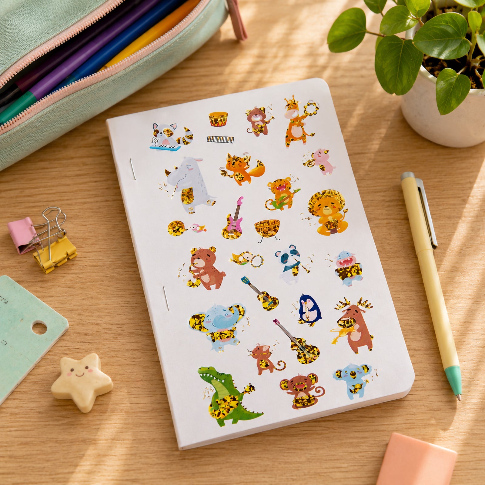 Sticker sheet displayed on a desk beside stationery, a pencil case and a potted plant. The holographic animal musicians perform with various instruments, demonstrating the vibrant colours and reflective foil finish across the collection.