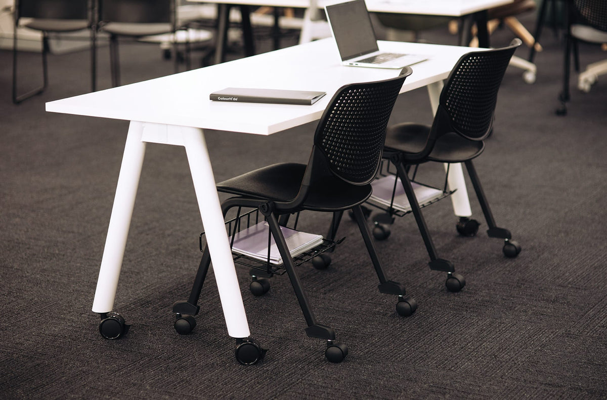 Black Konfurb Keen chairs at a white training table, each with an under seat basket holding notebooks and folders