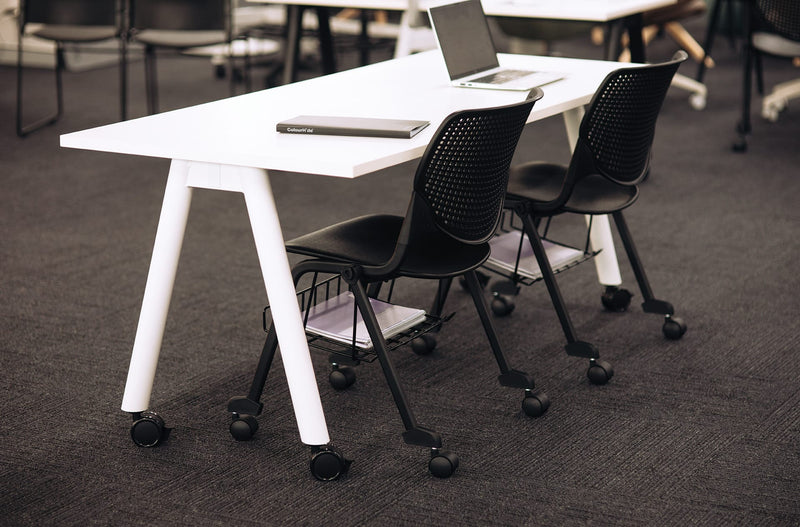 Black Konfurb Keen chairs at a white training table, each with an under seat basket holding notebooks and folders