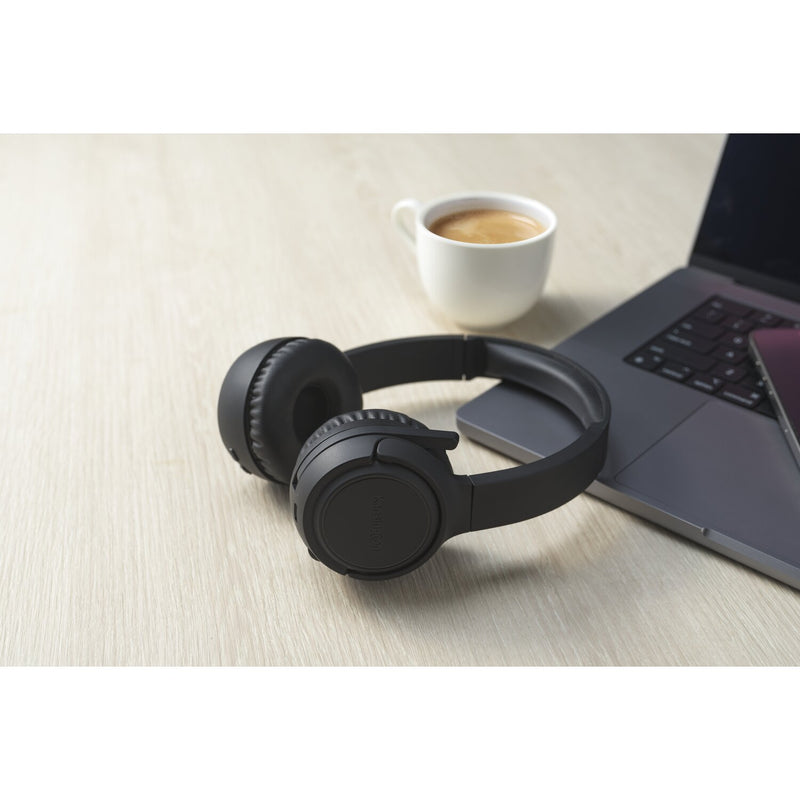 Kensington H1050 EQ Bluetooth headset on a timber desk beside a laptop and a cup of coffee