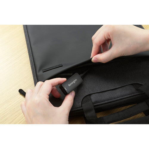 Hands slipping the compact Kensington CV4200H adapter into the front pocket of a black laptop bag
