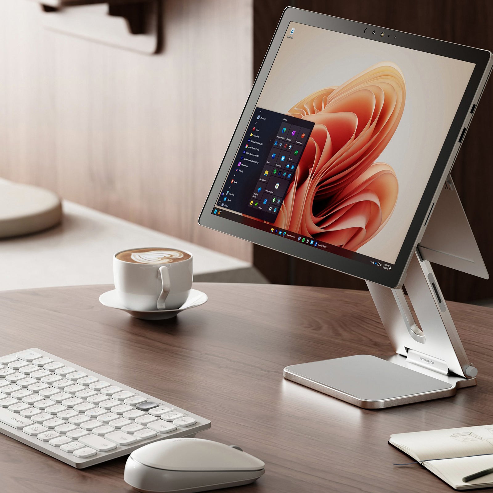 Close up workstation scene featuring a Microsoft Surface mounted on the Kensington Elevated Stand. The setup includes a wireless keyboard, mouse and coffee cup, highlighting ergonomic positioning and a clean professional workspace.