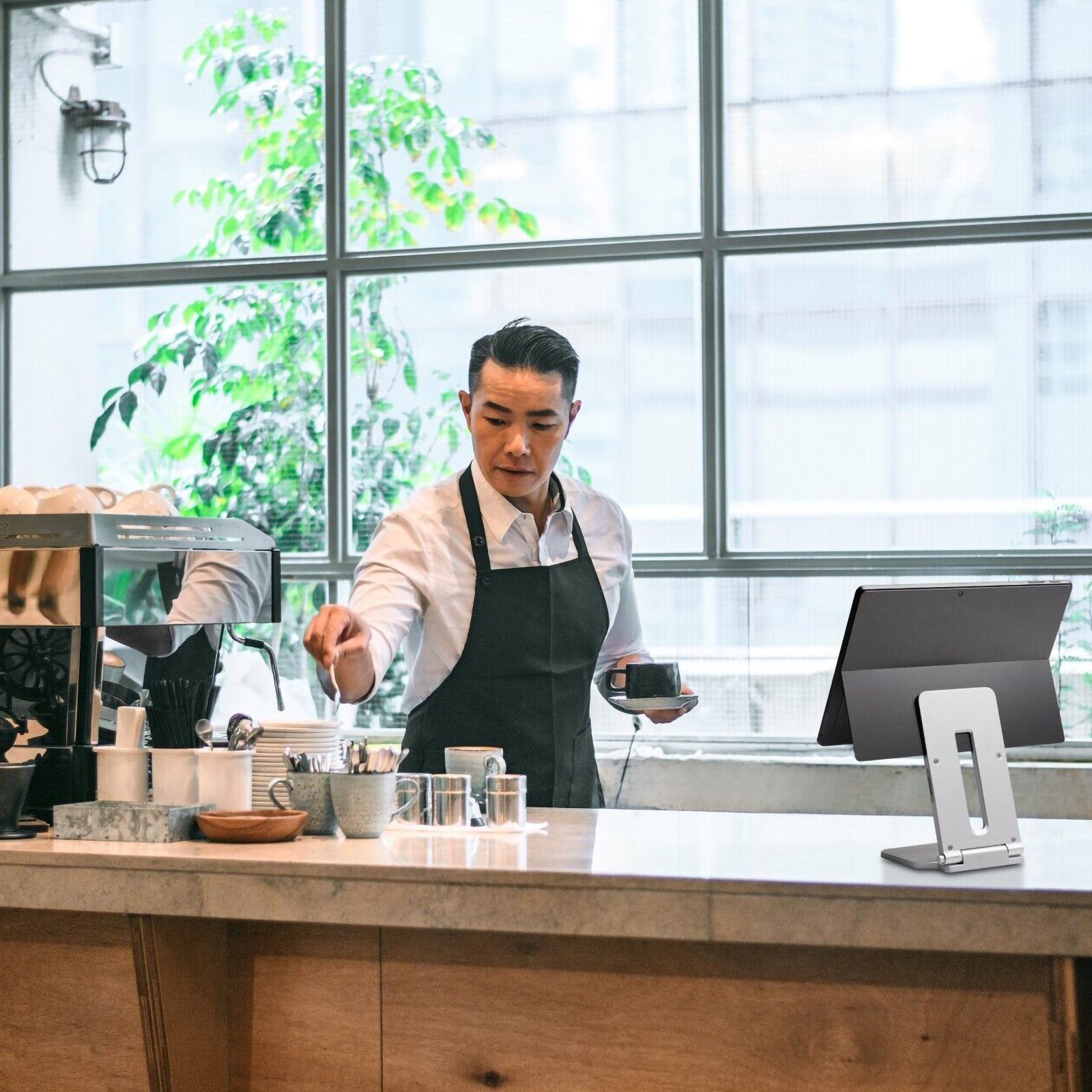 Kensington Elevated Stand for Microsoft Surface displayed in a modern cafe environment. A Surface device is positioned at a comfortable viewing angle on the premium aluminium stand, demonstrating its suitability for flexible workspaces, hospitality settings and mobile professionals.
