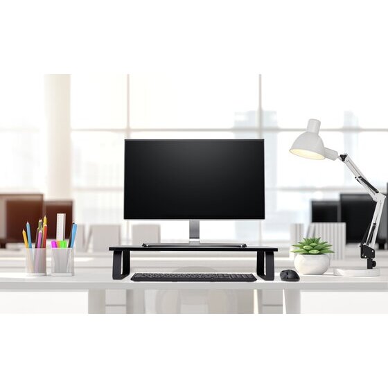 Office desk with a monitor raised on the black Kensington extra wide monitor stand beside a desk lamp and pot plant