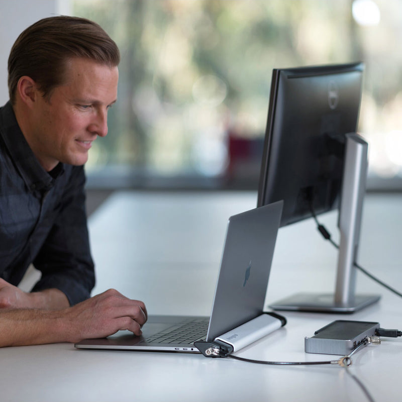 Professional workstation setup featuring a laptop secured within the Kensington Locking Station. The security cable is connected to a fixed point while the user works comfortably, demonstrating how the locking station protects valuable devices without interrupting productivity.