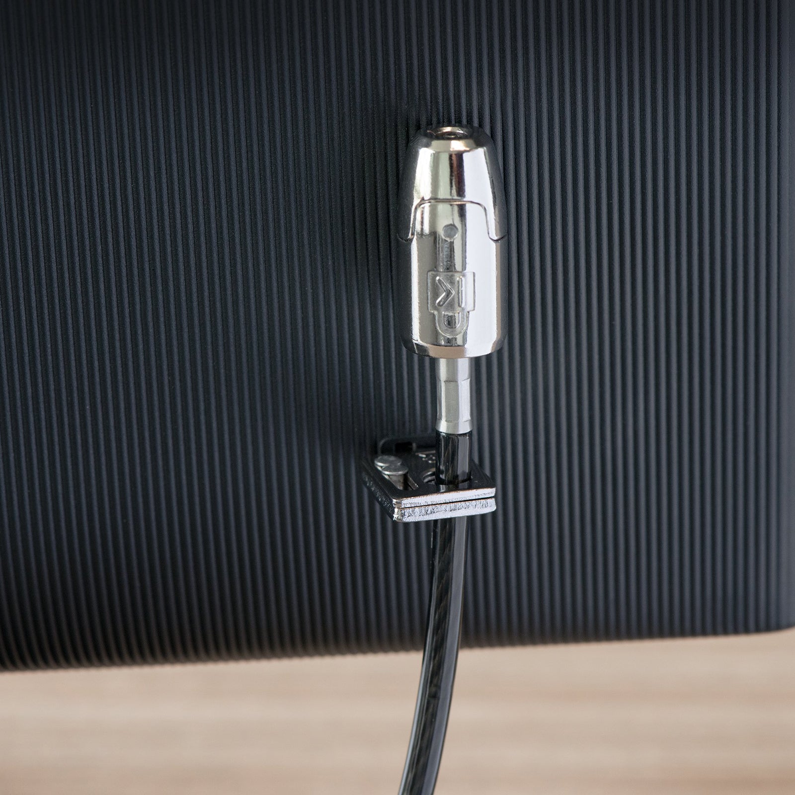 Close up of the Kensington T Bar lock head attached to a monitor security slot. The detailed view showcases the precision engineered lock mechanism and robust metal construction designed for professional device security.