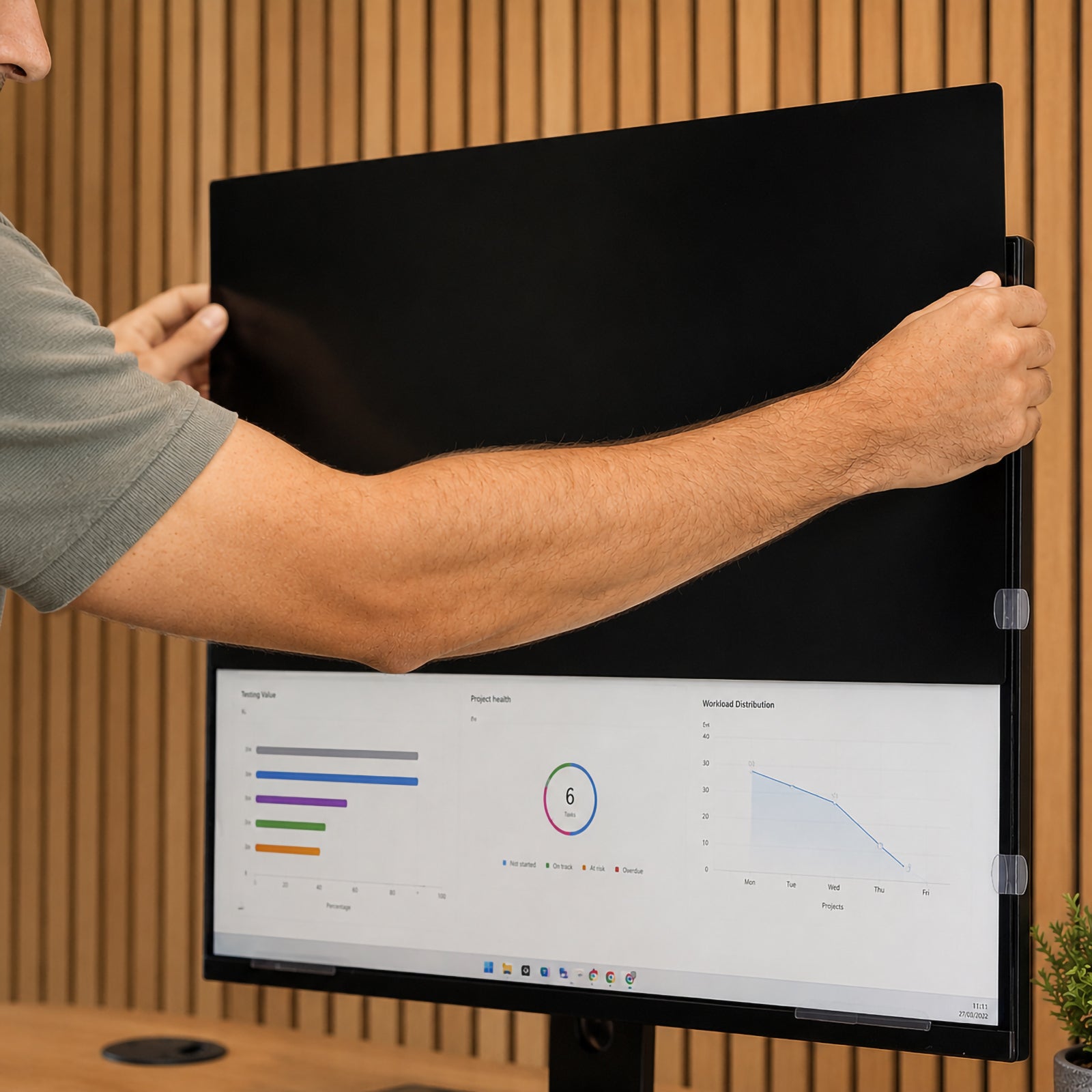 Close up image showing a user installing a Kensington privacy screen onto a 31.5 inch widescreen monitor using mounting tabs. The image highlights the simple installation process and secure fit designed for professional office displays.