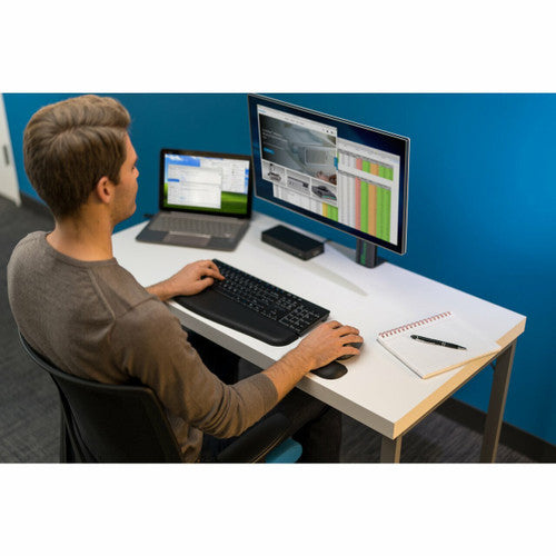 Man working at a desk with a keyboard, laptop and monitor, using a Kensington Pro Fit full size wireless mouse