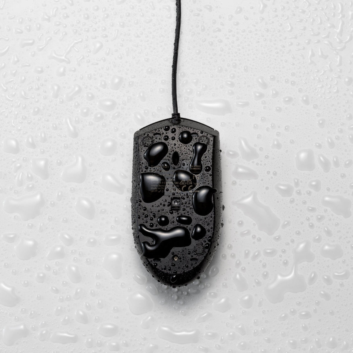 Black Kensington Pro Fit washable mouse lying on a wet surface with water droplets beaded across the shell