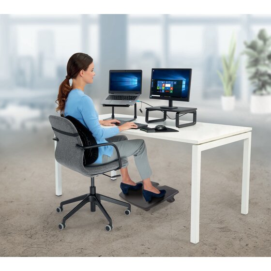 A person seated at a white desk with two monitors and both feet resting on a Kensington SoleRest foot rest under the desk