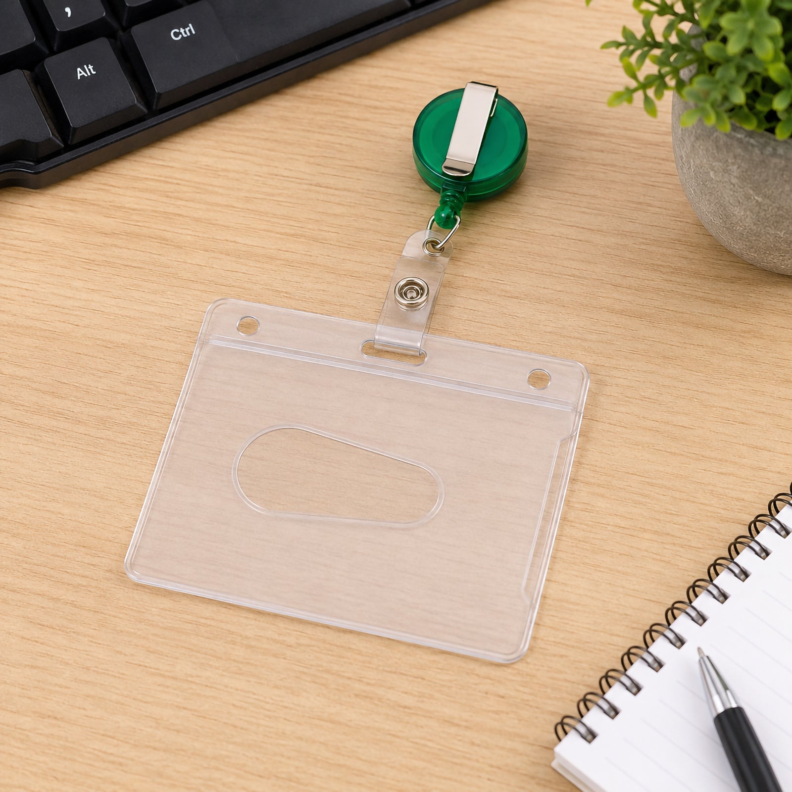 Rear view of the Kevron ID1013 clear ID card holder positioned on a desktop with the green retractable reel and sturdy metal clip visible. The image demonstrates the secure construction and rear slot designed for standard identification cards.