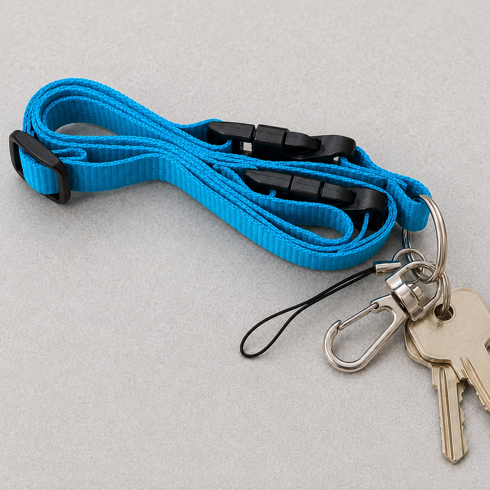 Close up view of the Kevron ID1047 blue multi use lanyard placed on a neutral surface with attached keys, a metal clip and a USB loop. The image highlights the durable woven strap, safety breakaway clip and versatile attachment options for carrying everyday essentials.