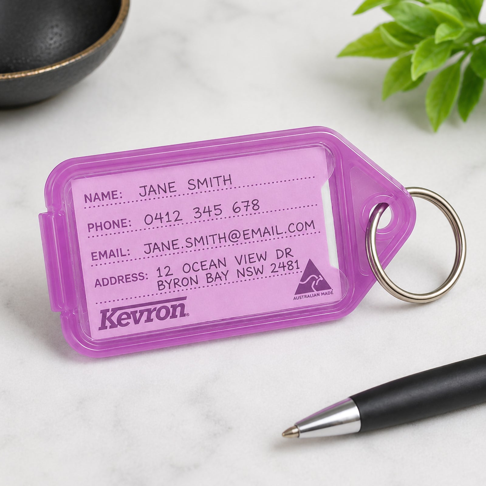 Close up of a Kevron ID30 Giant Key Tag in lilac displayed on a desktop beside a pen and decorative plant. The insert has been completed with sample contact details, highlighting the large writing area and excellent readability.