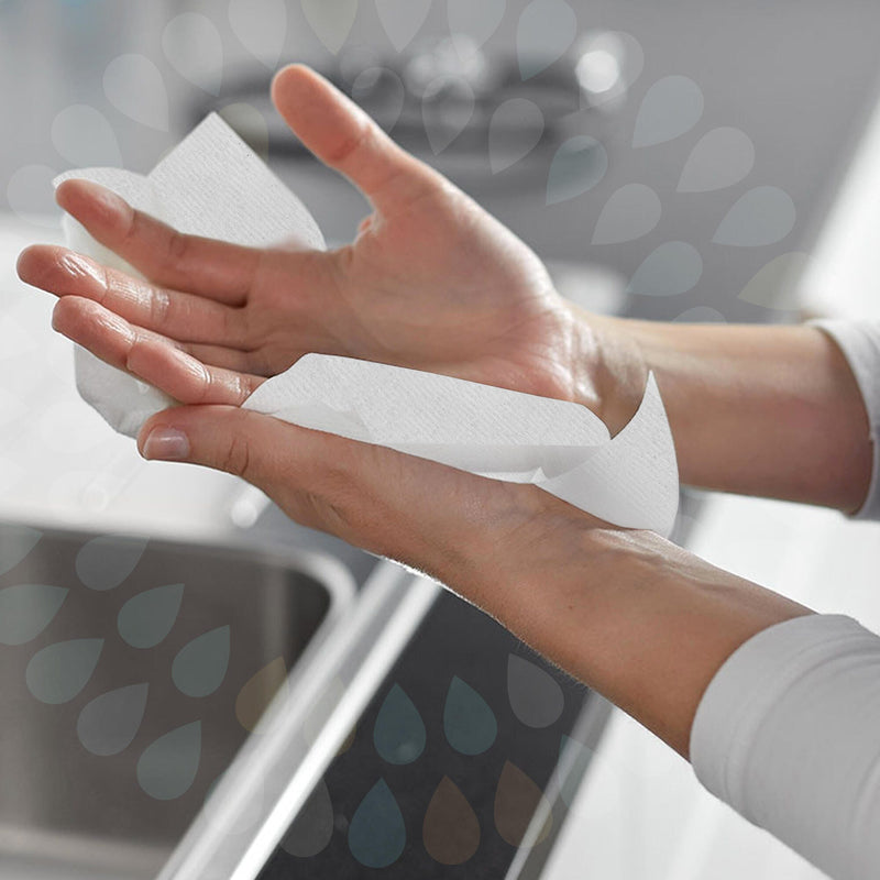 Close view of two wet hands being dried with a single white Kleenex compact hand towel at a washroom basin, showing the towel folded over the palm