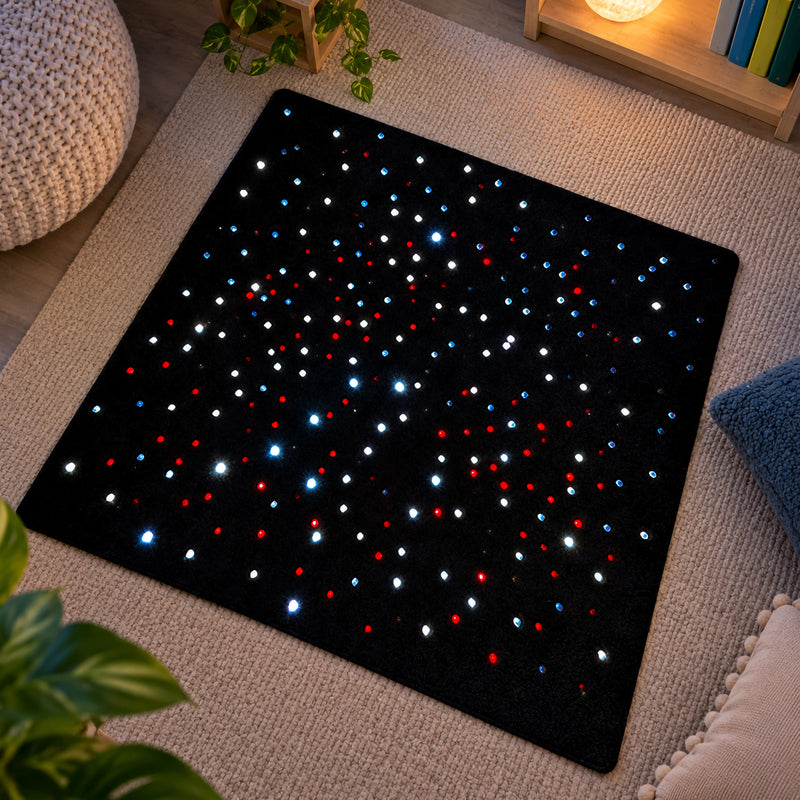 Top view of the MTA Essentials 95 x 95cm LED Sensory Carpet positioned in a quiet sensory environment. The black square carpet displays numerous glowing red, blue and white fibre optic points across its soft surface, demonstrating the visually engaging illuminated effect suitable for calm spaces, sensory rooms and supervised early learning activities.