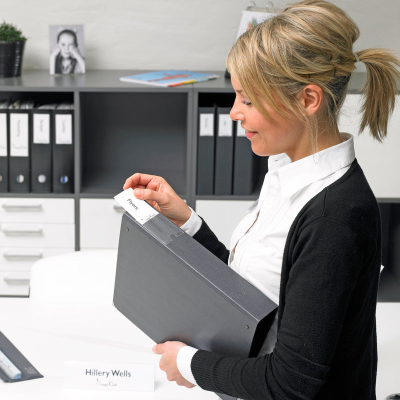 Office worker changing the insert in a 3L label holder on a black ring binder, with labelled binders on shelves behind