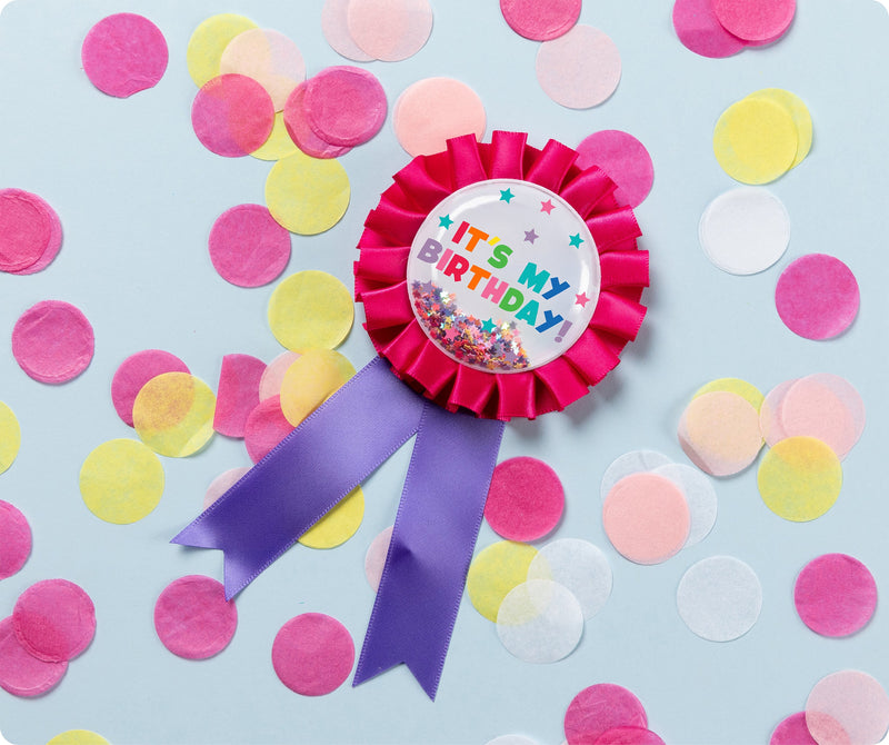 Pink Giggle and Grow birthday badge with a happy birthday message and loose metallic confetti visible inside the clear front pocket.