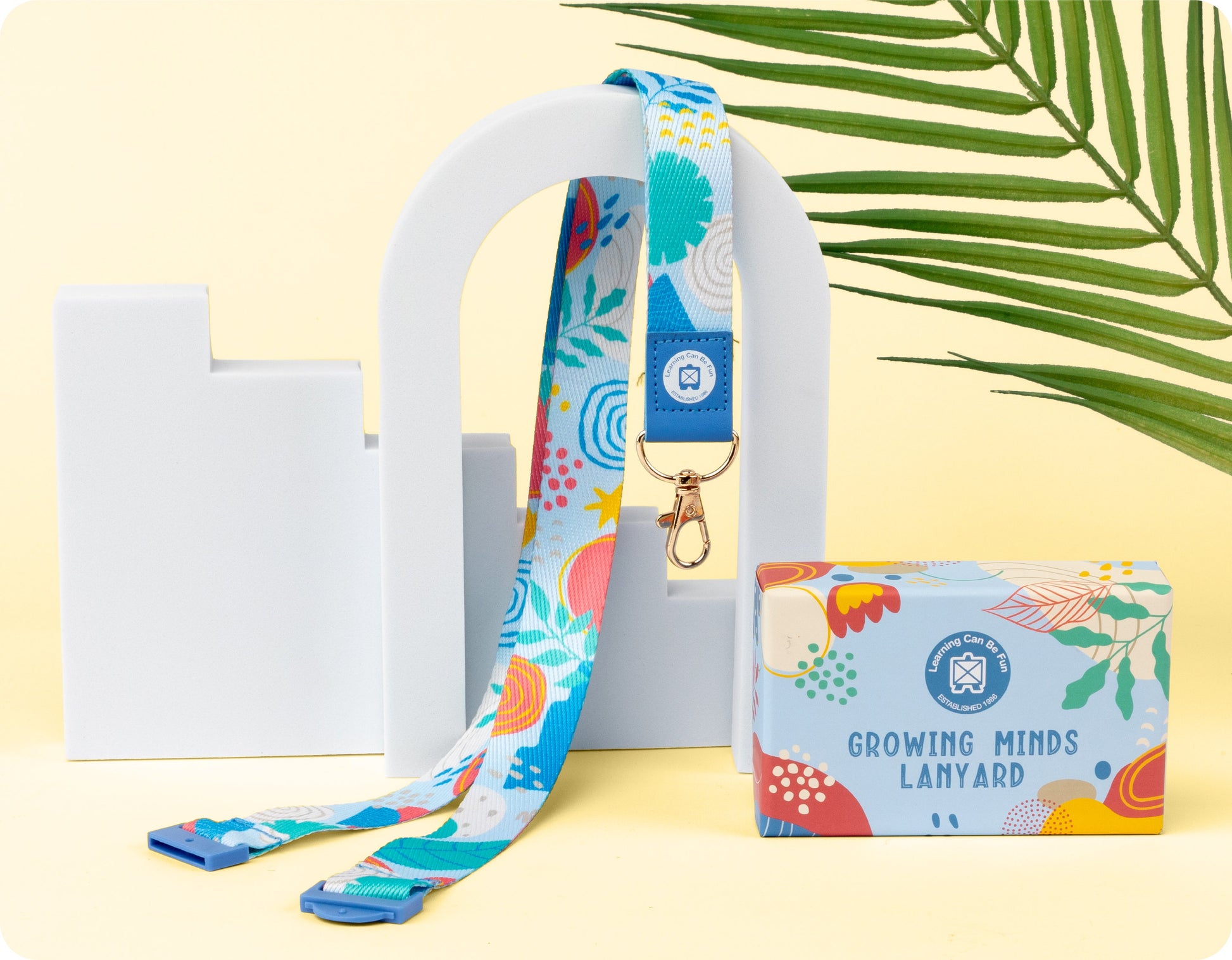 Growing Minds lanyard in neutral tones with a modern abstract shape print, shown flat with the clasp and safety breakaway clip visible.