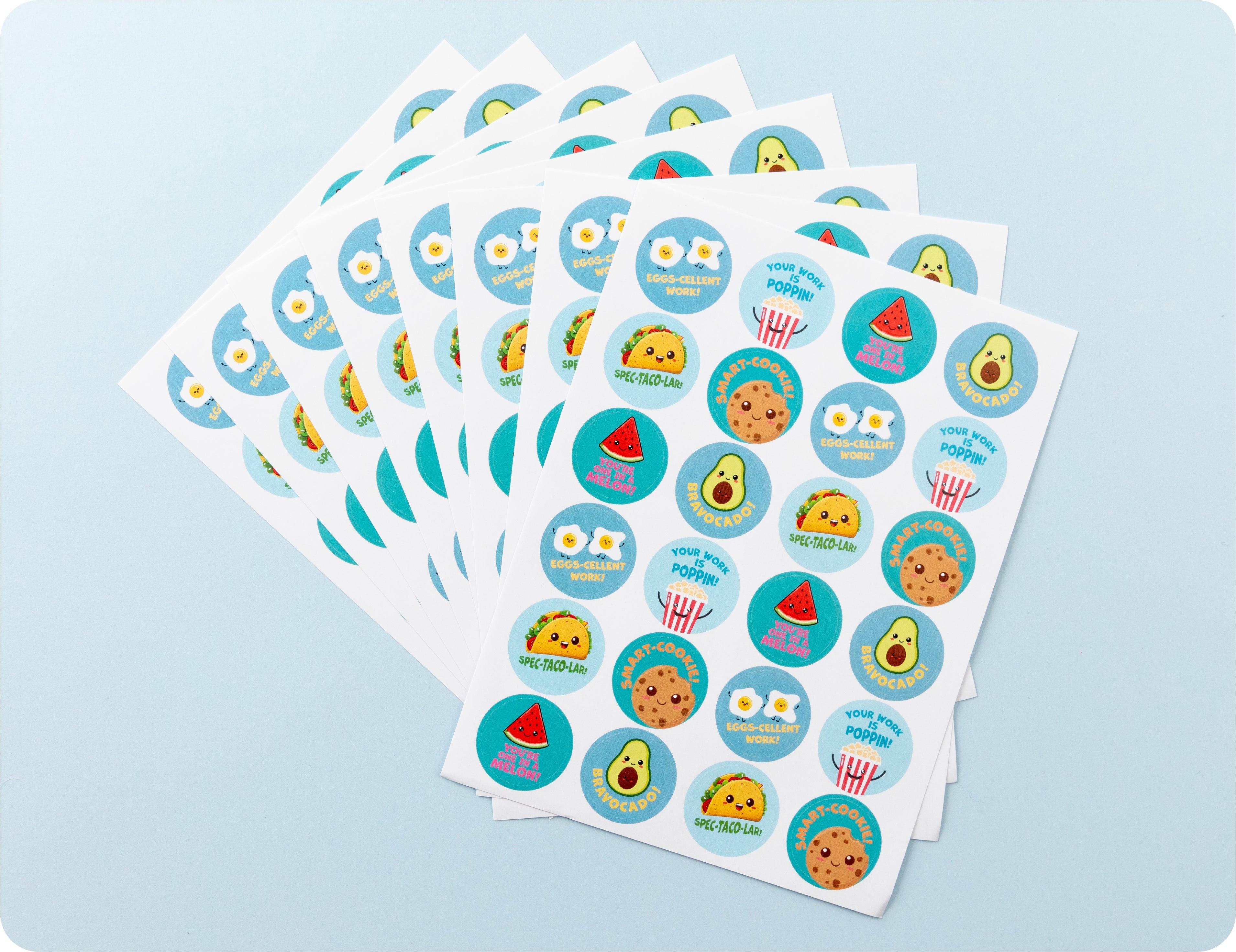 Sticker sheets from the Tasty Triumphs book fanned out to show the food character designs and pun phrases.
