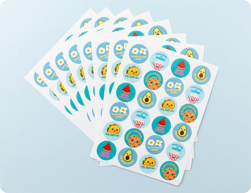 Sticker sheets from the Tasty Triumphs book fanned out to show the food character designs and pun phrases.