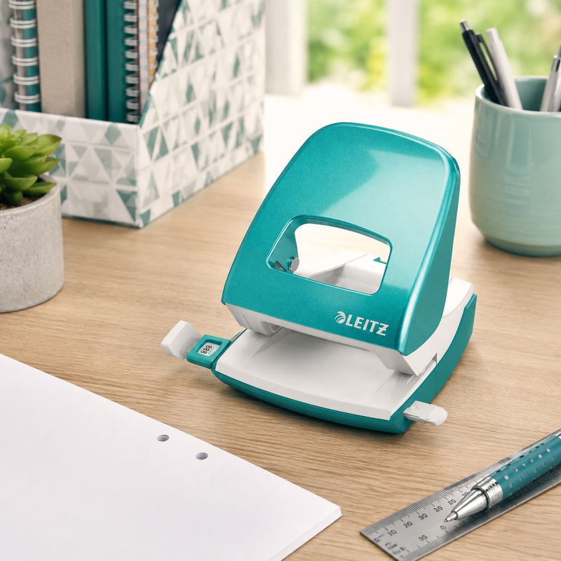 The Leitz NeXXt WOW 2 Hole Punch in Ice Blue is positioned on a wooden office desk beside organised files, stationery, a ruler and a pen. Natural daylight and office accessories create a productive workspace, emphasising the punch's stylish appearance and practical everyday use.