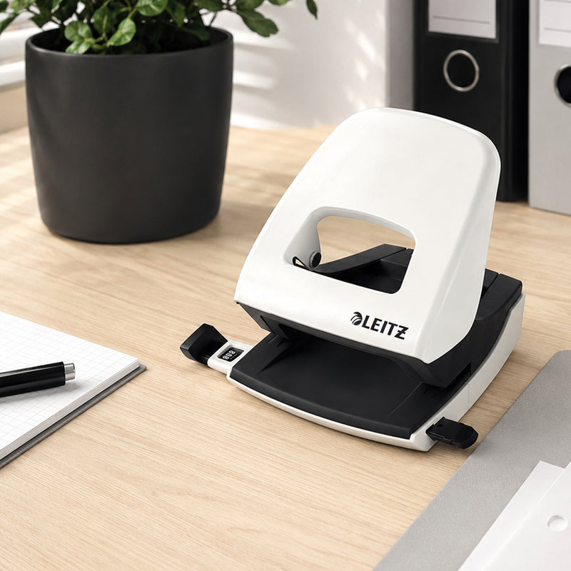 The Leitz NeXXt WOW 2 Hole Punch in White sits on a contemporary wooden desk beside a notebook, pen, office binders and an indoor plant. The lifestyle scene showcases its elegant appearance, durable construction and suitability for organised workspaces.