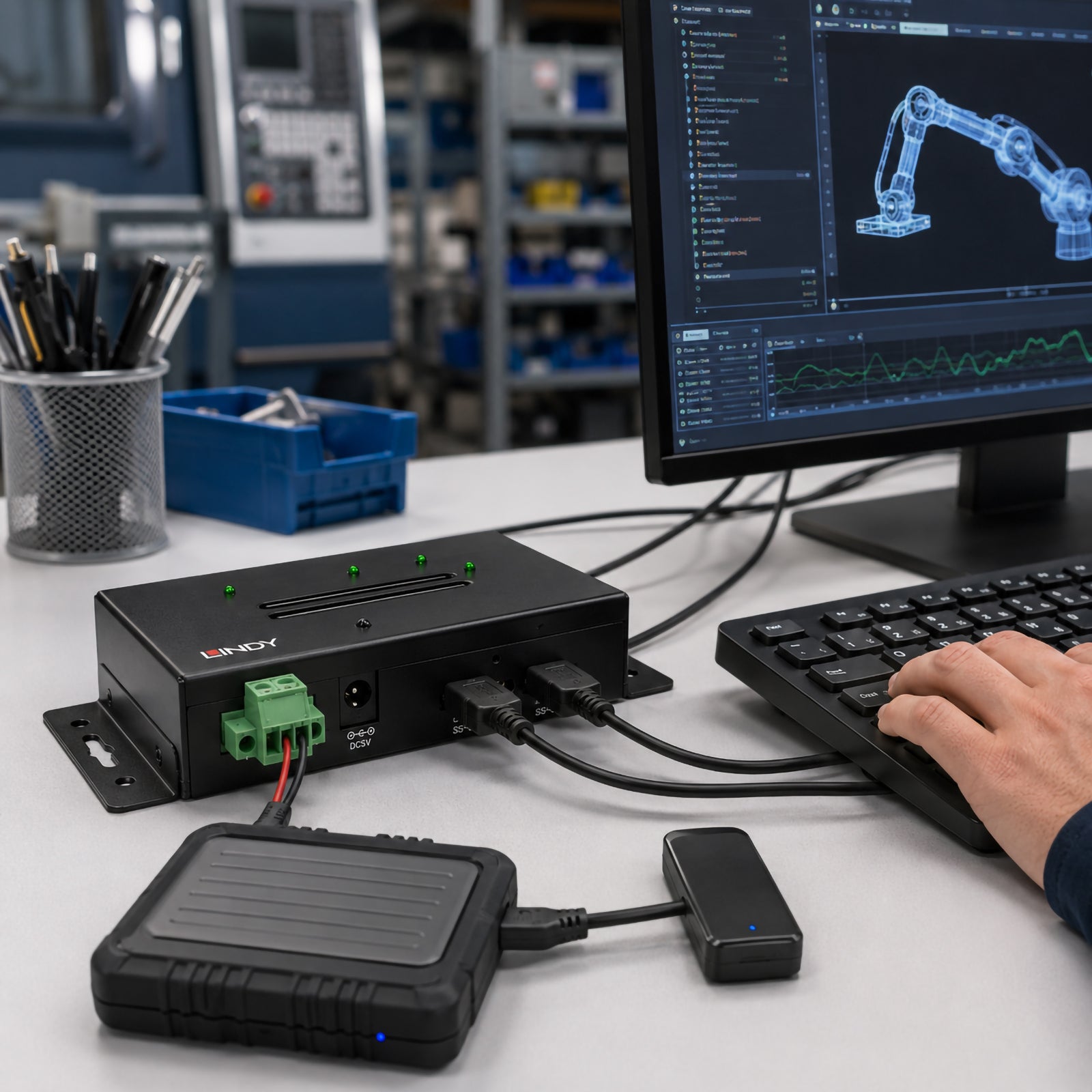 The Lindy 4 Port USB 3.2 Gen 2 Industrial Hub is installed on an industrial engineering workstation with connected USB devices, keyboard and computer monitor displaying engineering software. The image demonstrates the hub's rugged metal construction and suitability for factory automation, industrial control systems and high speed USB connectivity.