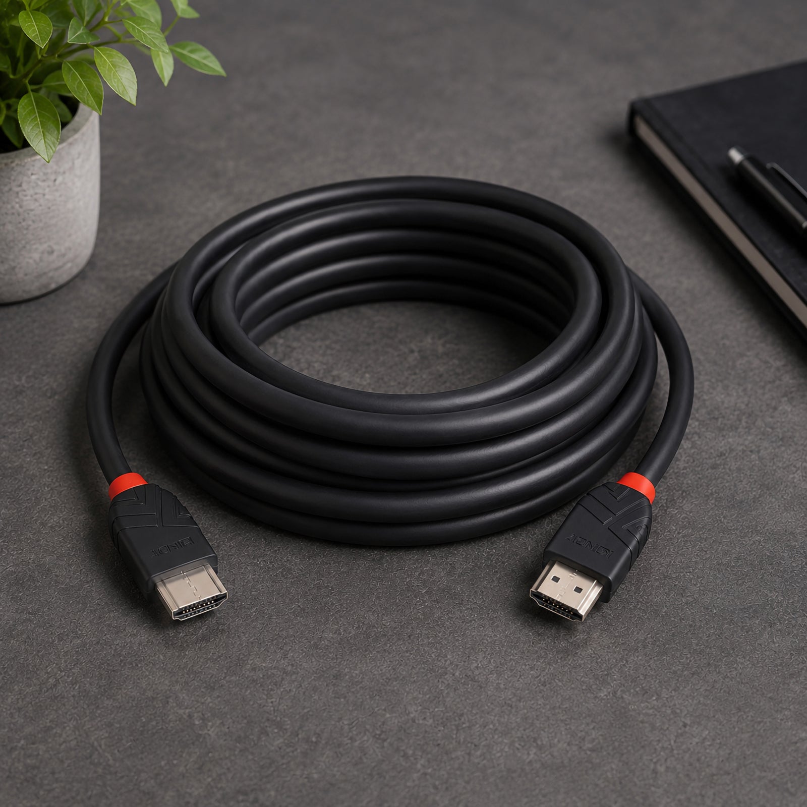 The Lindy 7.5m 8K60Hz HDMI Cable Black Line is neatly coiled on a modern desktop beside a notebook and indoor plant. Both HDMI Type A connectors are clearly visible, highlighting the flexible cable design and premium construction suitable for home entertainment and professional AV installations.