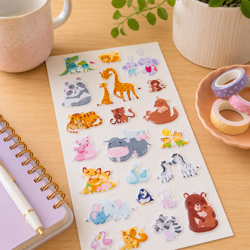 Full sticker sheet displayed on a desk with notebooks, washi tape and stationery accessories. The collection features 22 raised animal stickers including bears, giraffes, zebras, elephants, foxes and other caring animal characters.