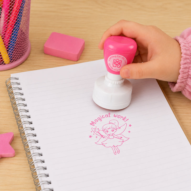 A child uses the Magical Work Merit Stamp on a notebook page, creating a bright pink fairy themed impression with the Magical Work! message. The image highlights the easy self inking operation and demonstrates how teachers can provide positive feedback in a fun and engaging way.