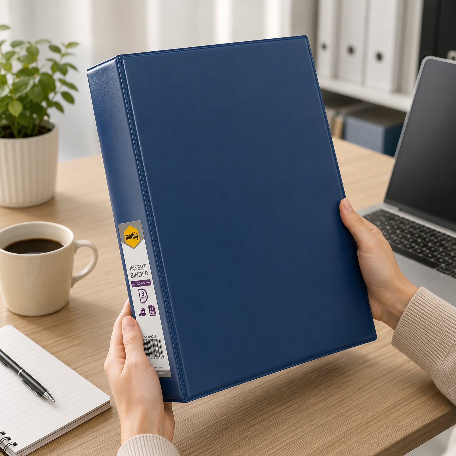 Hands holding the Marbig Clearview A4 50mm 3D Ring Blue Insert Binder in a contemporary office beside a laptop, coffee cup and notebook, showcasing comfortable handling and professional document organisation during everyday work.