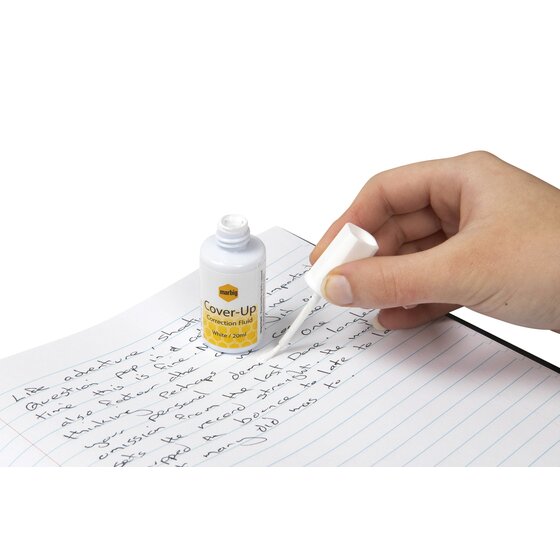Hand brushing Marbig Cover-Up correction fluid onto handwriting on lined paper, with the open 20ml bottle beside it