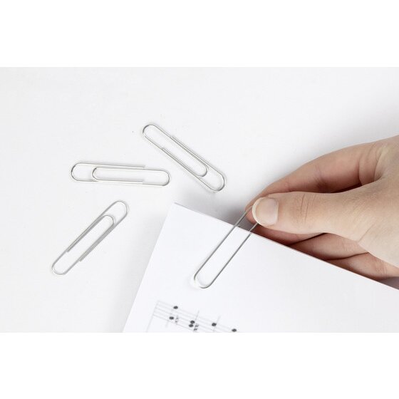 Hand fitting a long silver Marbig 50mm paper clip over the edge of a sheet of music, three more clips beside it