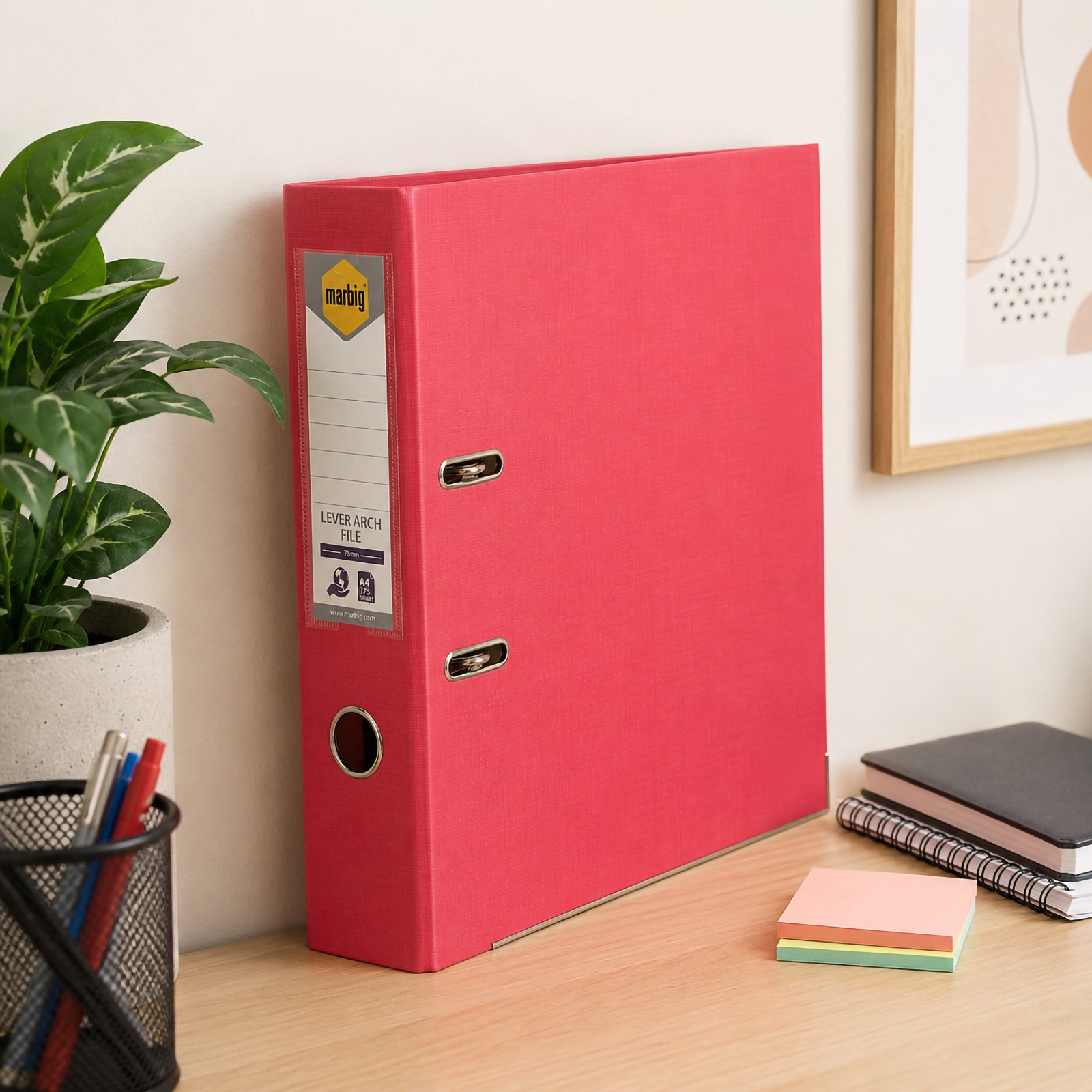 Marbig Lever Arch File A4 PE Coral standing upright on an office desk beside notebooks, plants and stationery, demonstrating its attractive colour, sturdy construction and organised office storage.