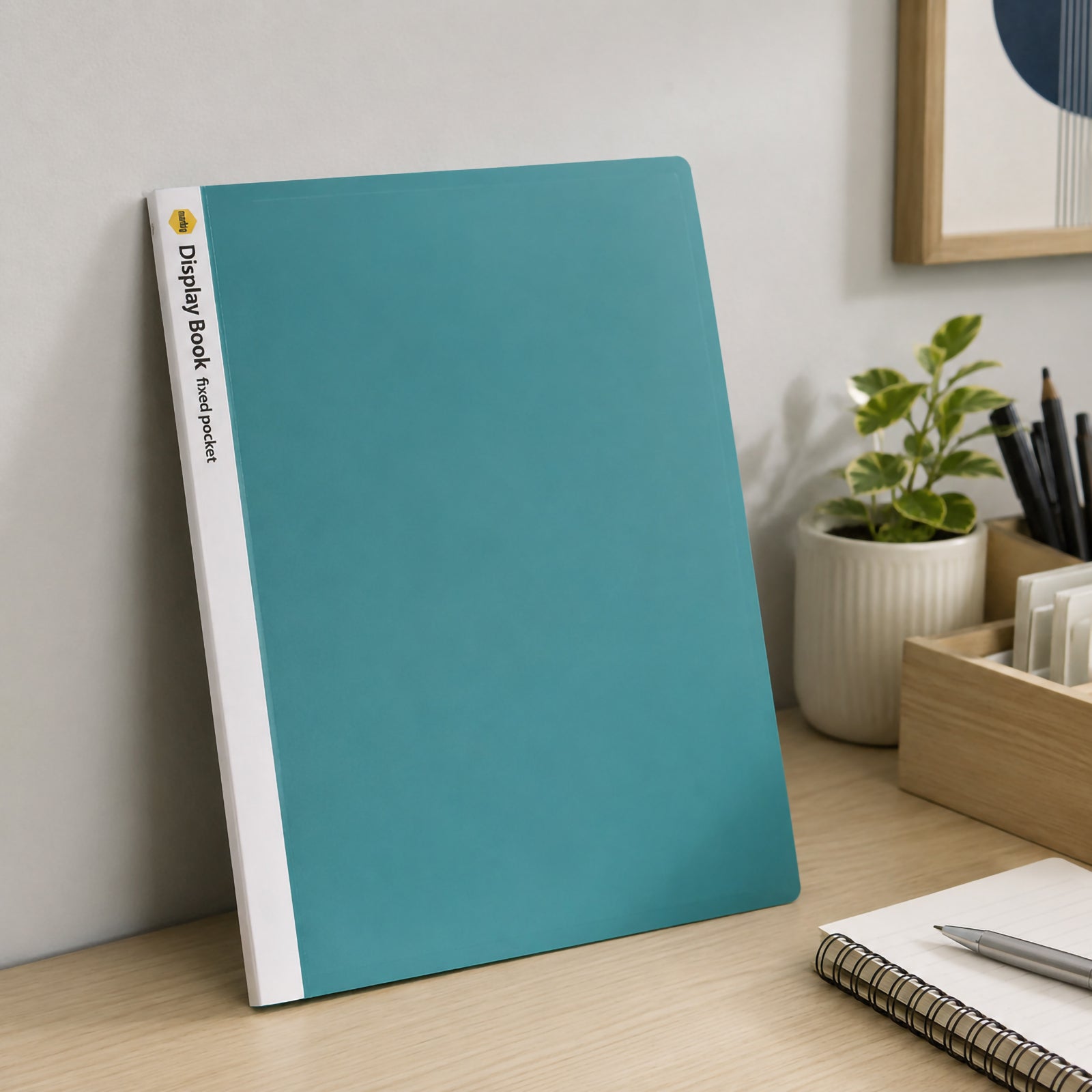 Marbig A4 green display book standing upright against an office wall on a timber desk beside stationery, a notebook and indoor plant. The clean office environment demonstrates practical everyday storage for reports, presentations and business documents.