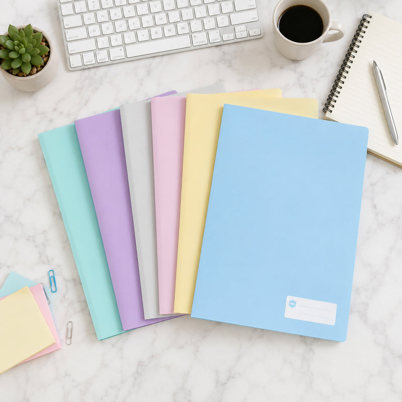 Top view of six Marbig A4 pastel assorted display books arranged across a marble desktop beside a keyboard, notebook, coffee cup and stationery. The soft blue, yellow, pink, mint, grey and lavender covers demonstrate an organised colour coded filing system.