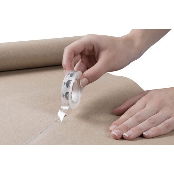 Hand pulling a strip of Marbig clear office tape from the roll across a sheet of brown kraft paper