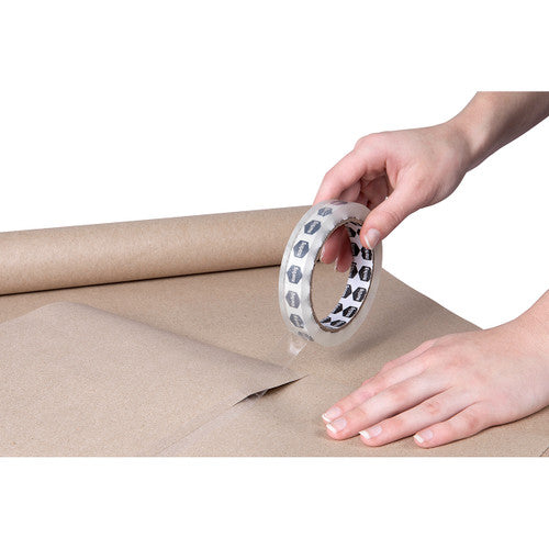 Hand pressing a Marbig clear tape roll onto a sheet of brown kraft paper on a table