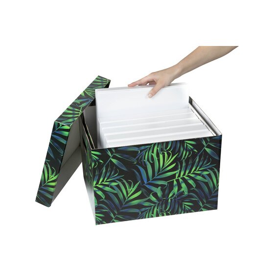 Hand placing white binders into an open Marbig Midnight Palm archive box with the palm print lid tilted back
