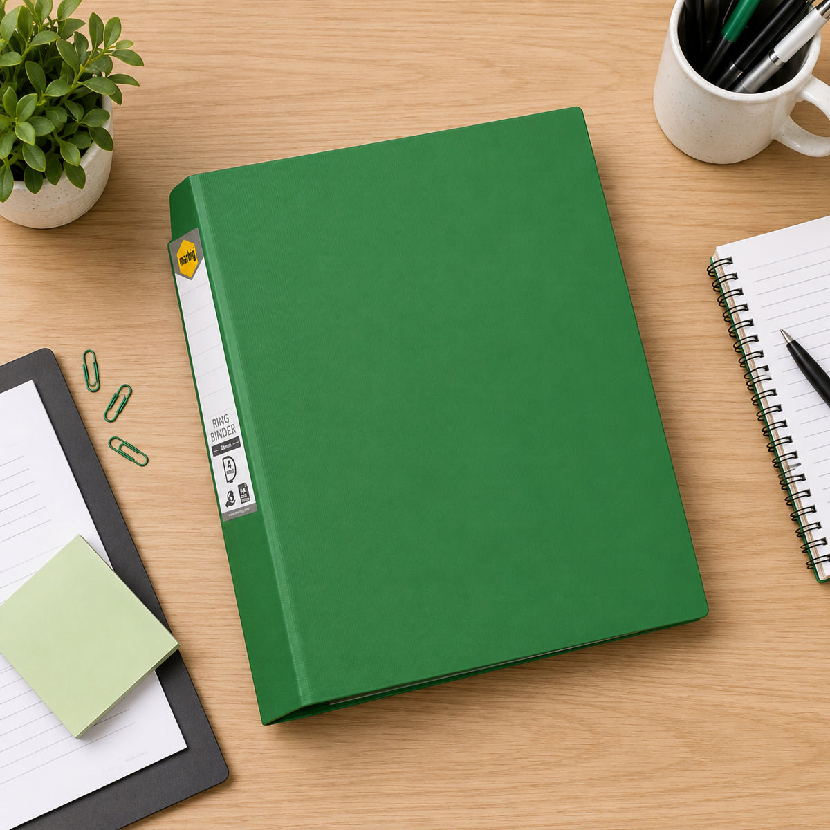 Green Marbig ring binder lying closed on a desk seen from above, with a notebook and sticky notes nearby