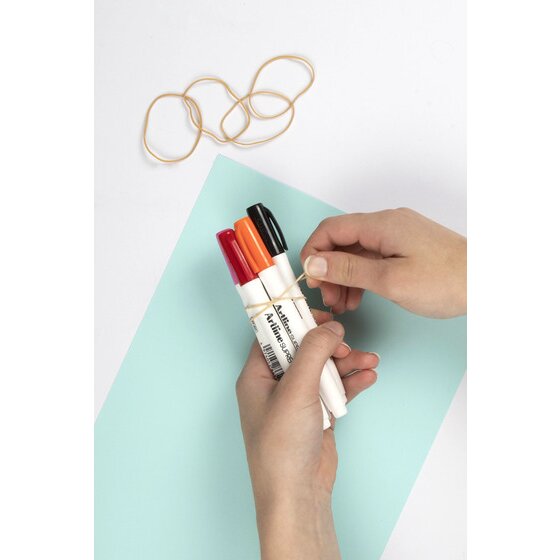 Hands wrapping a natural coloured rubber band around a bundle of red, orange and black marker pens on a pale green sheet
