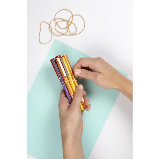 Hands wrapping a natural coloured rubber band around a bundle of marker pens, with loose bands resting on the page above