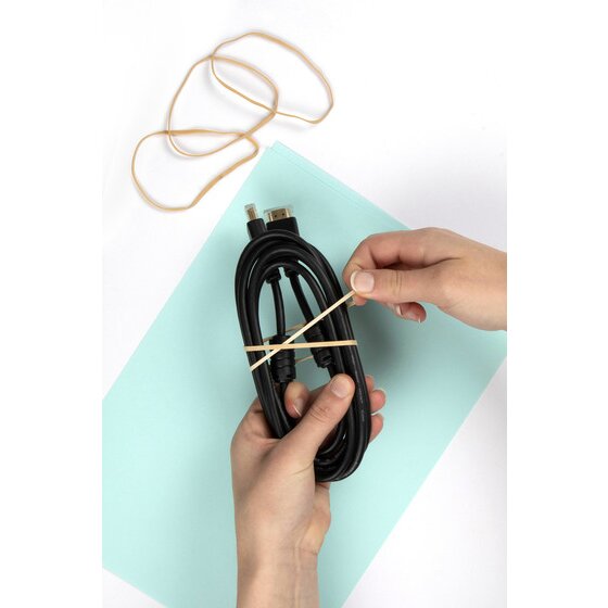 Hands wrapping a natural rubber band around a coiled black cable lying on a pale blue sheet of card
