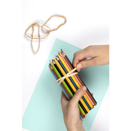 Hands binding a bundle of coloured pencils with a natural rubber band on a pale blue sheet of card
