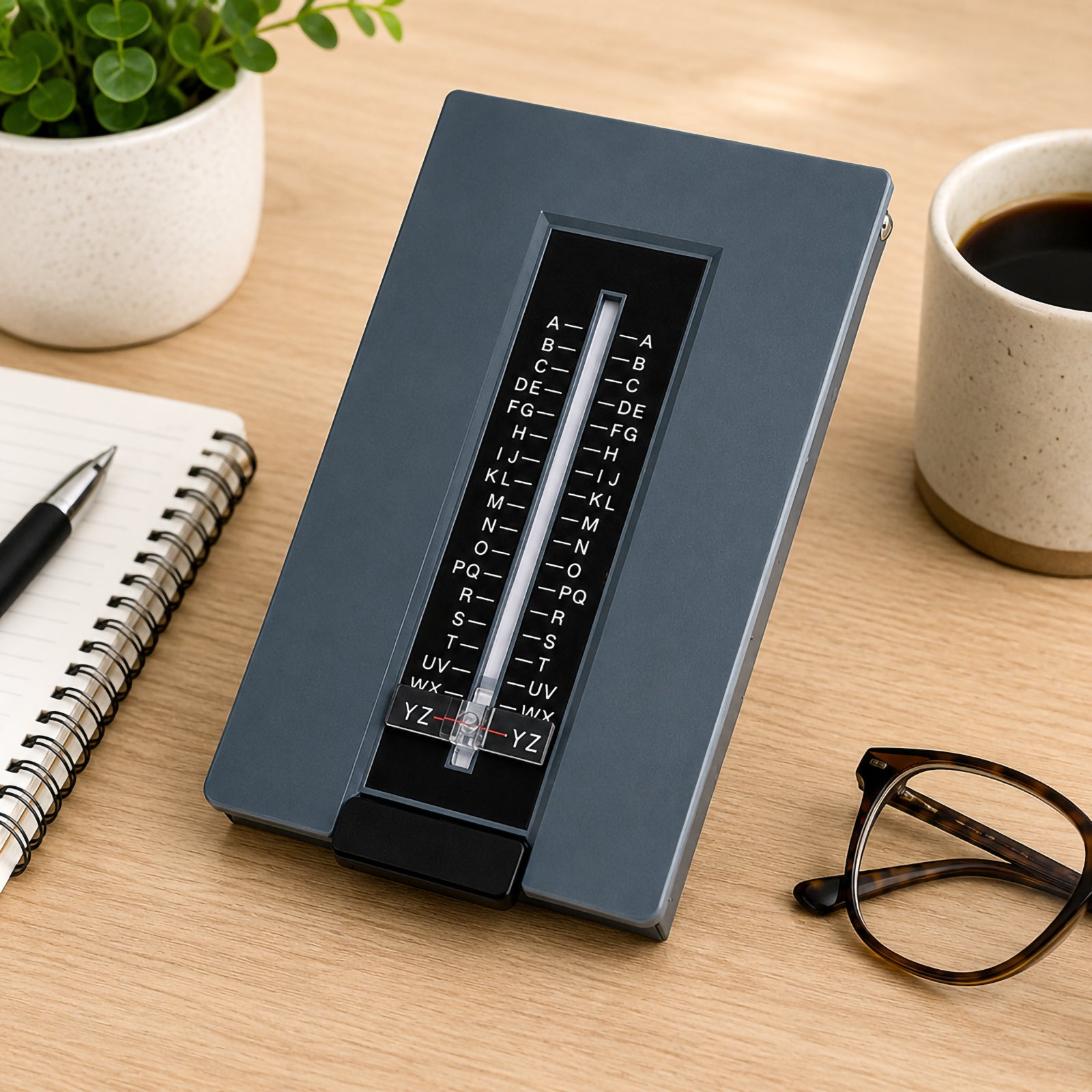 Closed Marbig Telephone List Finder Grey displayed on a timber desk next to a notebook, coffee cup and reading glasses, showcasing the sleek grey finish and easy to use alphabetical viewing window.